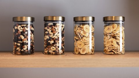 Bilder aus der Sportalm Vier Gläser mit Nüssen und Bananenchips auf einem Holzregal