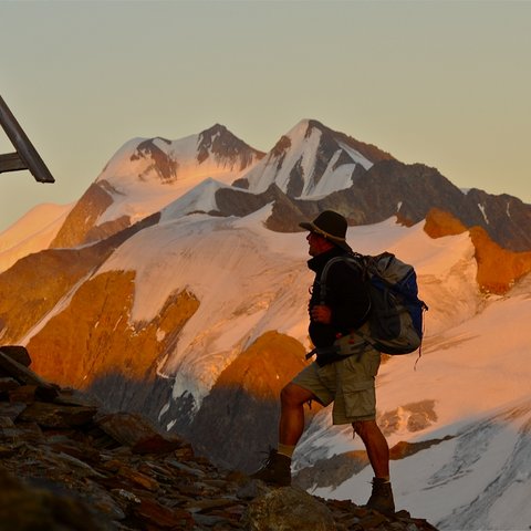 Pictures from Sportalm Hiker with backpack on mountain trail next to wooden cross at sunset