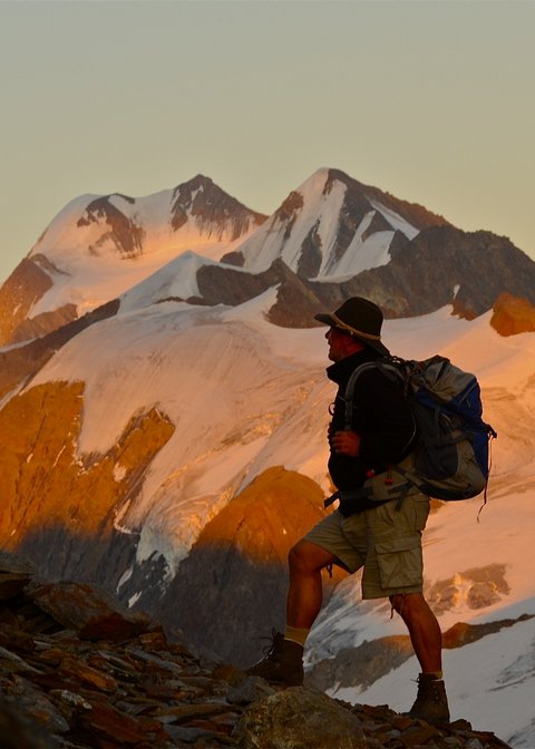 Pictures from Sportalm Hiker with backpack on mountain trail next to wooden cross at sunset