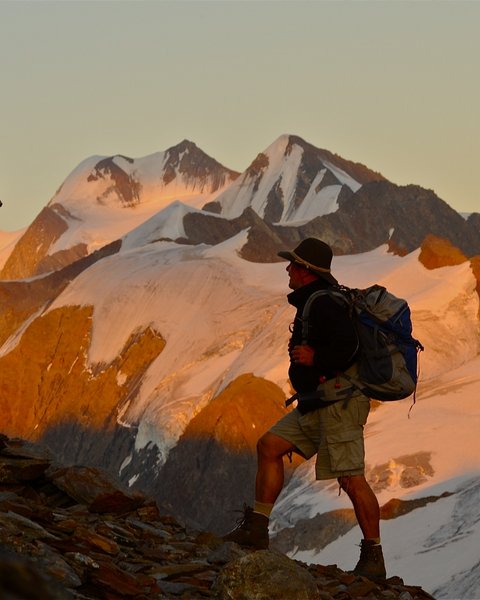 Pictures from Sportalm Hiker with backpack on mountain trail next to wooden cross at sunset