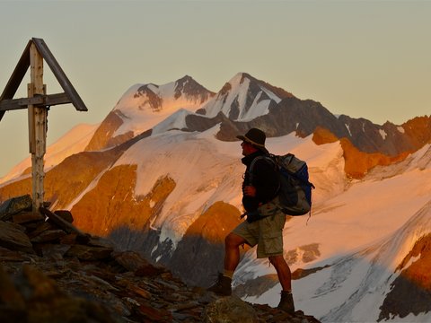 Pictures from Sportalm Hiker with backpack on mountain trail next to wooden cross at sunset
