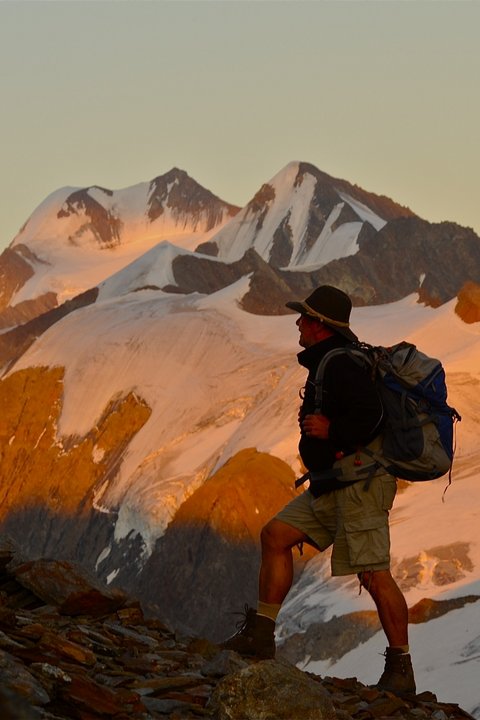 Pictures from Sportalm Hiker with backpack on mountain trail next to wooden cross at sunset