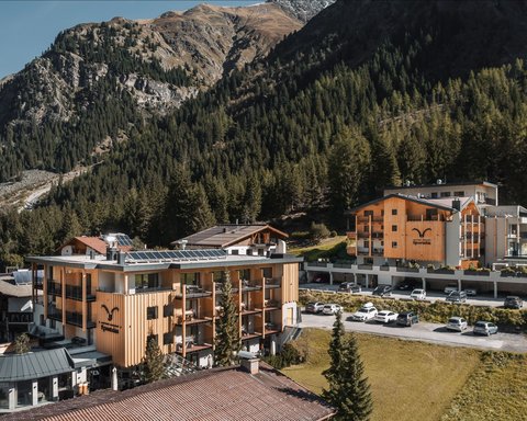 Bilder aus der Sportalm Hotelgebäude umgeben von Bergen und Wäldern an einem sonnigen Tag