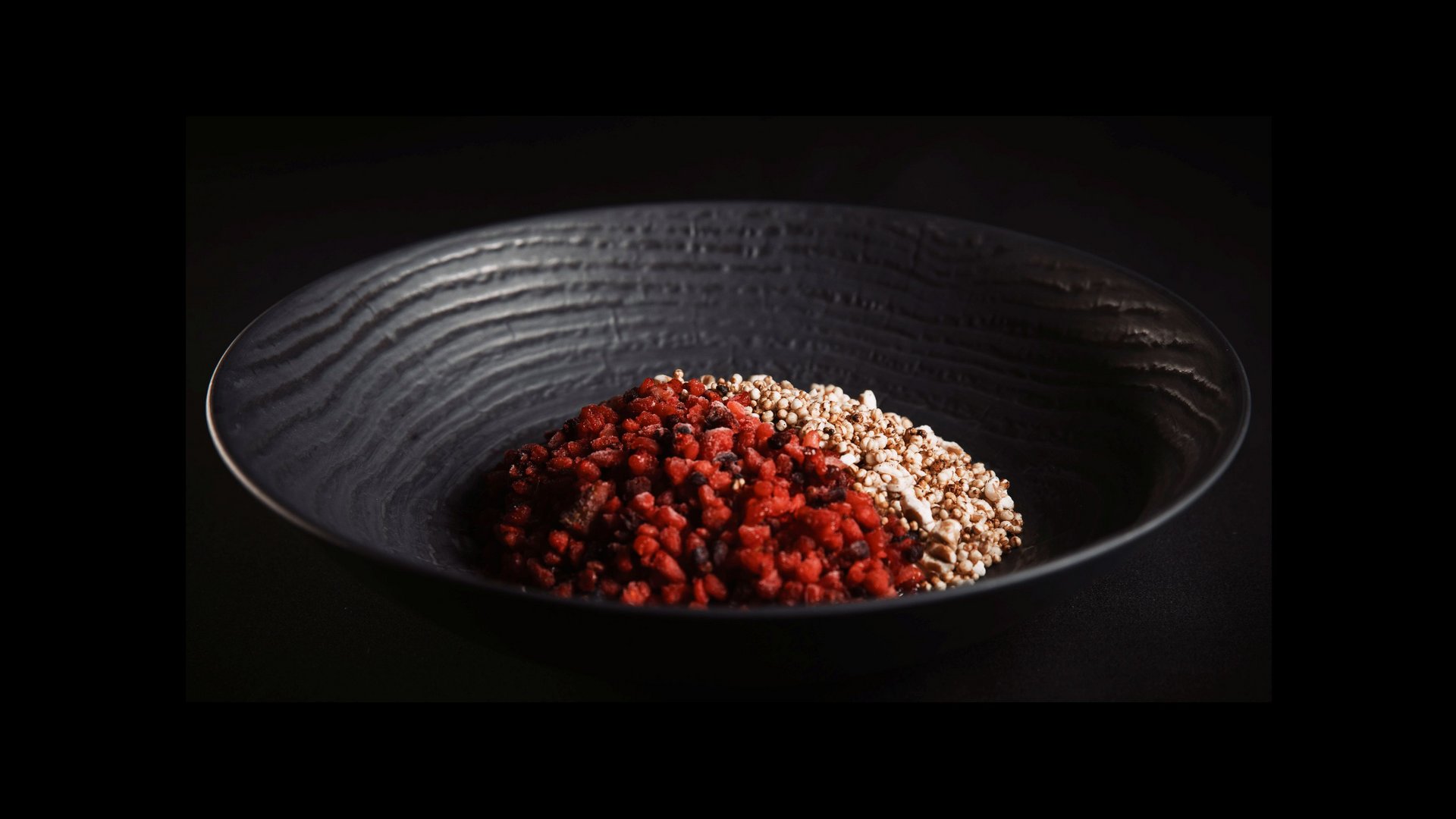 Our restaurant in Pitztal Black bowl with half red and half white granular ingredients on black background