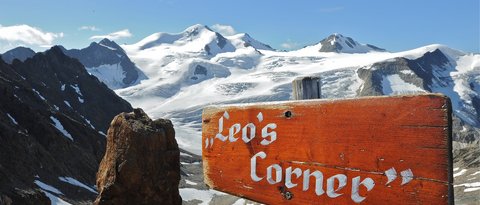 Bilder aus der Sportalm Holzschild Leo's Corner vor schneebedeckten Bergen und blauem Himmel