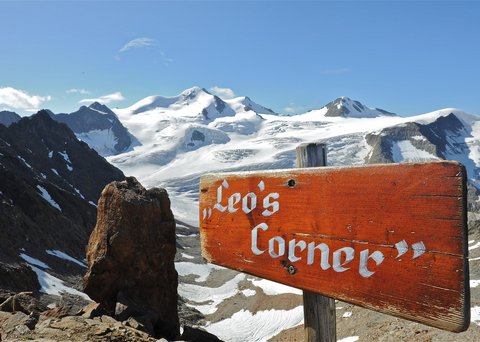 Bilder aus der Sportalm Holzschild Leo's Corner vor schneebedeckten Bergen und blauem Himmel