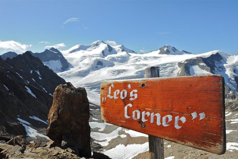 Bilder aus der Sportalm Holzschild Leo's Corner vor schneebedeckten Bergen und blauem Himmel