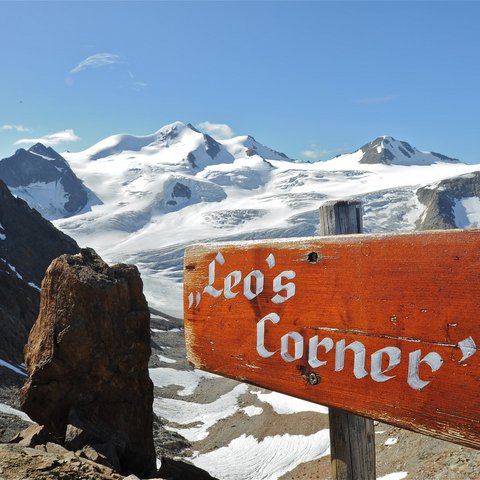 Bilder aus der Sportalm Holzschild Leo's Corner vor schneebedeckten Bergen und blauem Himmel