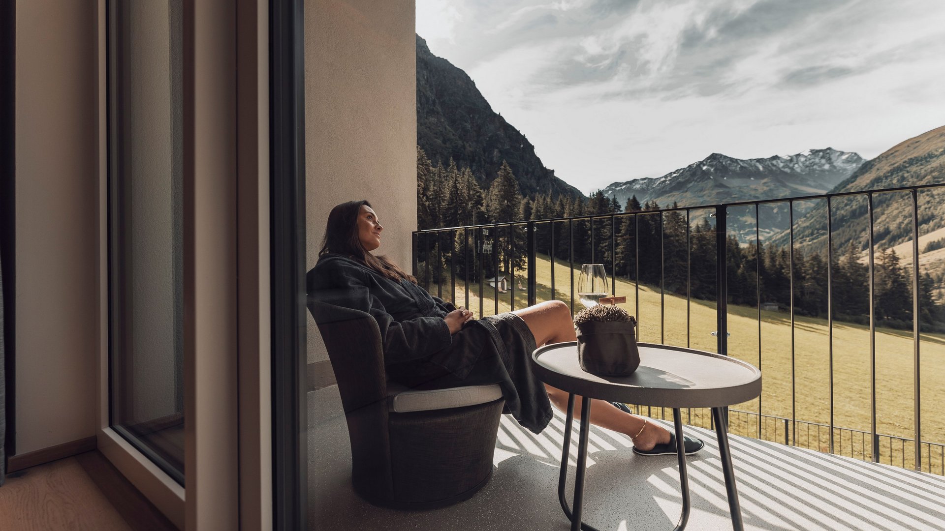 Live aus St. Leonhard im Pitztal Frau entspannt auf Balkon mit Bergblick in Morgenmantel