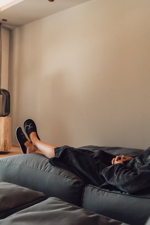 Bilder aus der Sportalm Frau entspannt sich auf Sofa in hellem Raum mit Kerzenlicht