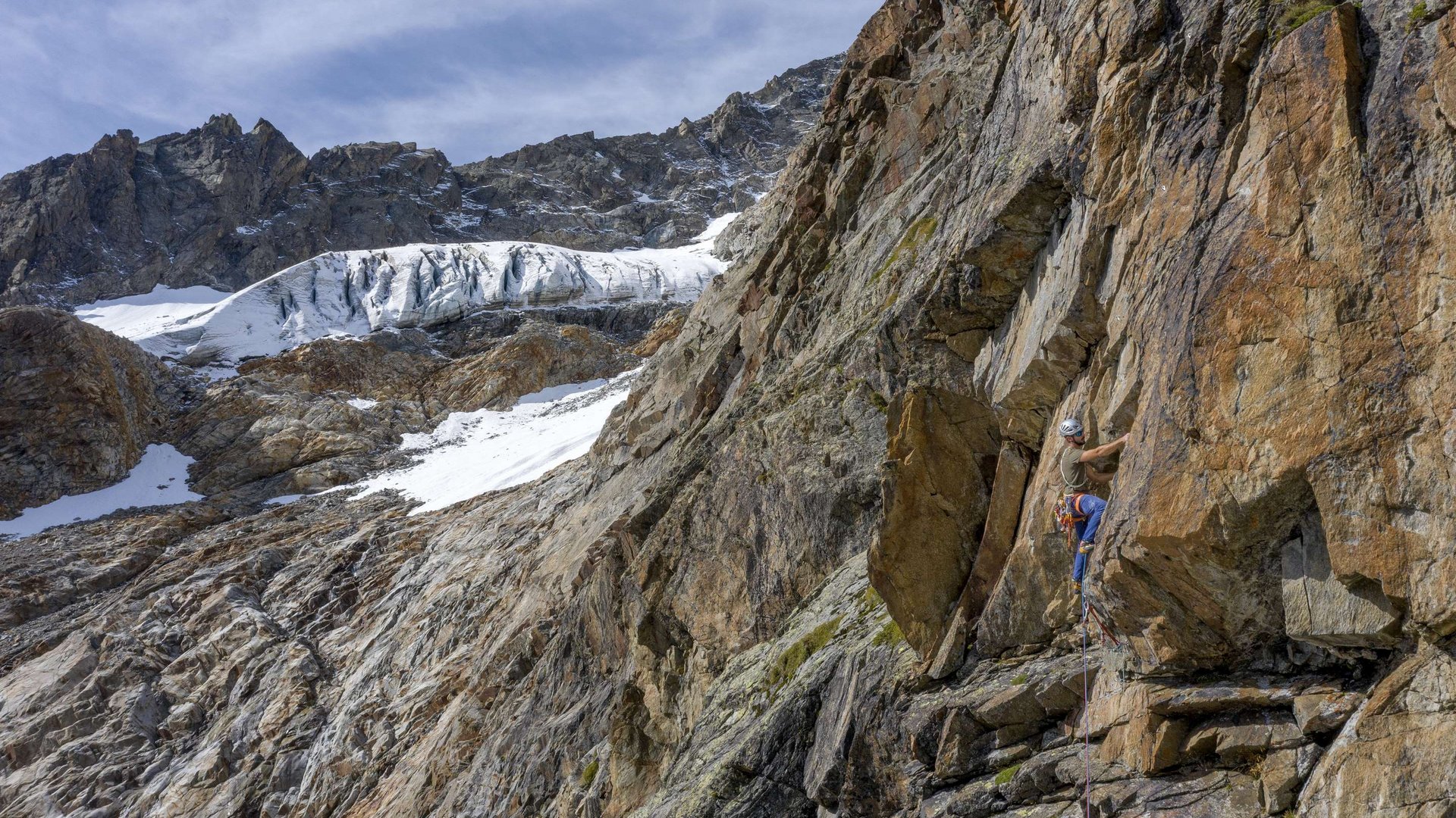 Kletterer an steiler Felswand mit schneebedecktem Berg im Hintergrund