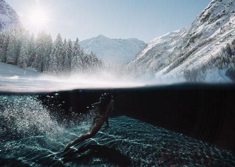 Pictures from Sportalm Woman swimming in clear water with snowy mountains and sunlight in background