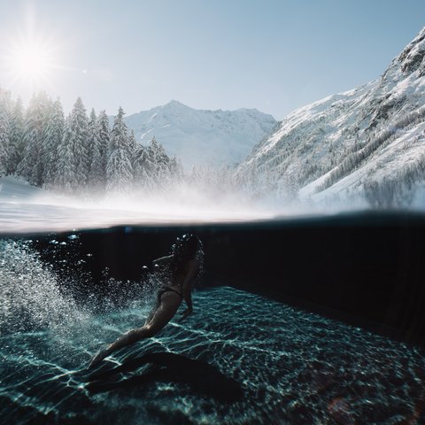 Pictures from Sportalm Woman swimming in clear water with snowy mountains and sunlight in background