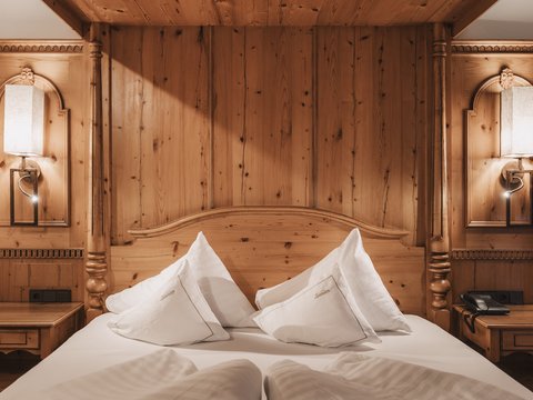 Bilder aus der Sportalm Gemütliches Holzbett mit weißen Kissen und Nachttischen mit Lampen