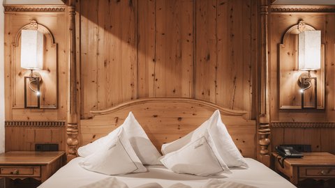 Bilder aus der Sportalm Gemütliches Holzbett mit weißen Kissen und Nachttischen mit Lampen