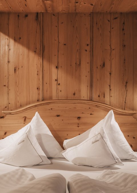 Bilder aus der Sportalm Gemütliches Holzbett mit weißen Kissen und Nachttischen mit Lampen