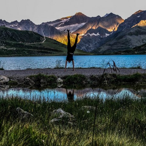 Pictures from Sportalm Person doing handstand by mountain lake with sunlight on peaks