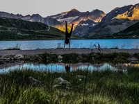 Person macht Handstand vor Bergsee mit Sonnenlicht auf Bergen