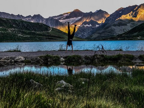 Bilder aus der Sportalm Person macht Handstand vor Bergsee mit Sonnenlicht auf Bergen