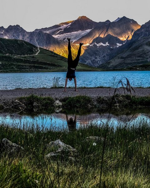 Bilder aus der Sportalm Person macht Handstand vor Bergsee mit Sonnenlicht auf Bergen