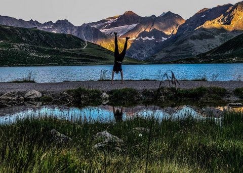 Pictures from Sportalm Person doing handstand by mountain lake with sunlight on peaks