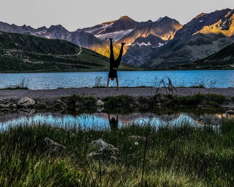 Bilder aus der Sportalm Person macht Handstand vor Bergsee mit Sonnenlicht auf Bergen