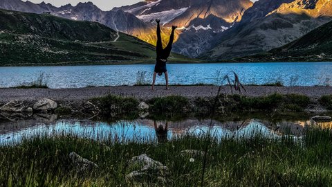 Bilder aus der Sportalm Person macht Handstand vor Bergsee mit Sonnenlicht auf Bergen