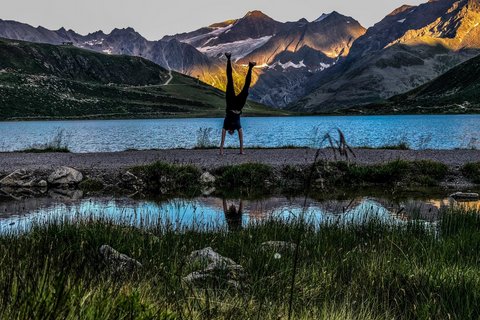 Bilder aus der Sportalm Person macht Handstand vor Bergsee mit Sonnenlicht auf Bergen