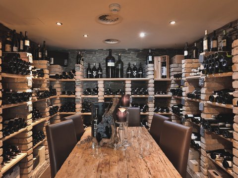 Our restaurant in Pitztal Wine cellar with wooden table, candles, and wine bottles on brick shelves