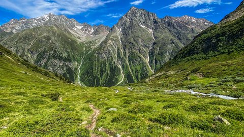 Bilder aus der Sportalm Wanderweg durch grüne Wiesen zu hohen Bergen unter blauem Himmel