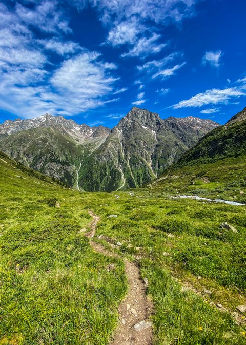 Bilder aus der Sportalm Wanderweg durch grüne Wiesen zu hohen Bergen unter blauem Himmel