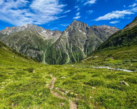 Bilder aus der Sportalm Wanderweg durch grüne Wiesen zu hohen Bergen unter blauem Himmel