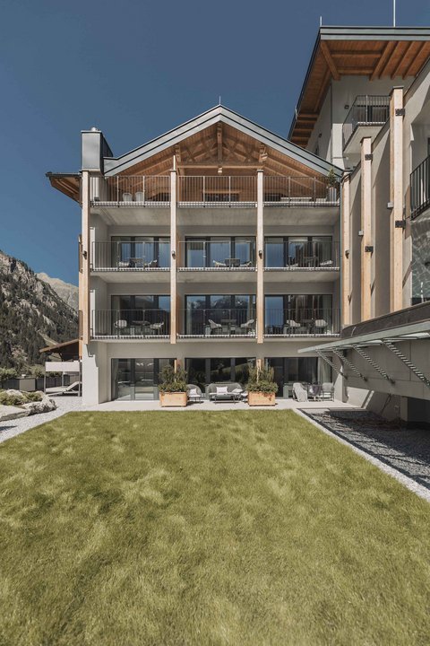 Bilder aus der Sportalm Modernes Hotelgebäude mit Balkonen vor einer Berglandschaft und grünem Rasen