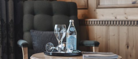 Pictures from Sportalm Armchair beside table with water bottle, glasses and book in wooden room