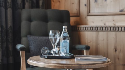 Bilder aus der Sportalm Sessel neben Tisch mit Wasserflasche, Gläsern und einem Buch in einem Holzraum