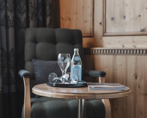Pictures from Sportalm Armchair beside table with water bottle, glasses and book in wooden room