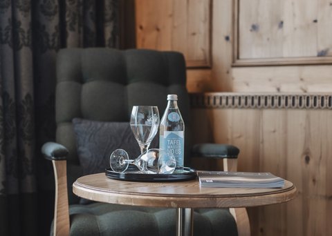 Bilder aus der Sportalm Sessel neben Tisch mit Wasserflasche, Gläsern und einem Buch in einem Holzraum