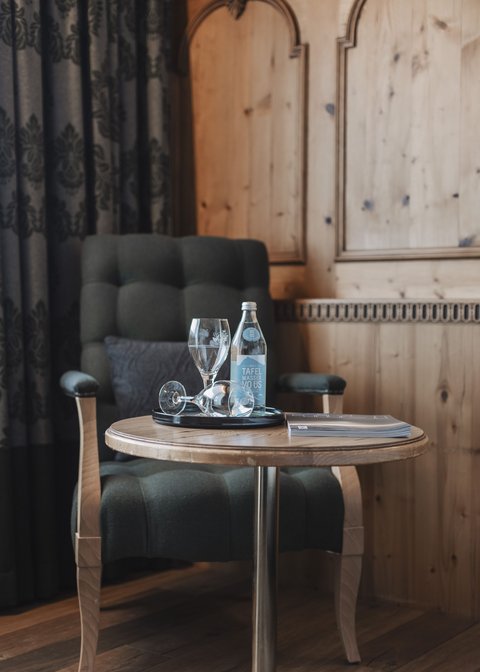 Bilder aus der Sportalm Sessel neben Tisch mit Wasserflasche, Gläsern und einem Buch in einem Holzraum