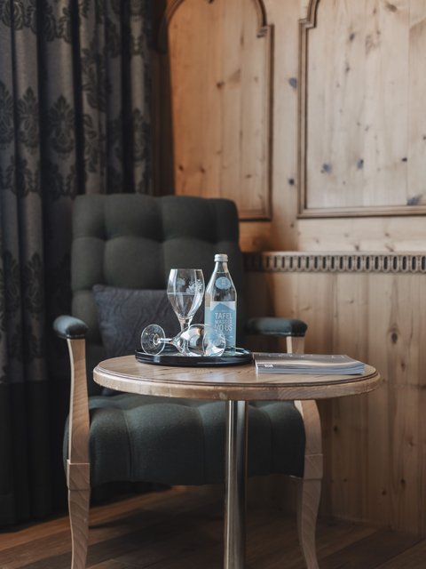 Bilder aus der Sportalm Sessel neben Tisch mit Wasserflasche, Gläsern und einem Buch in einem Holzraum