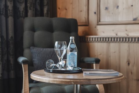 Bilder aus der Sportalm Sessel neben Tisch mit Wasserflasche, Gläsern und einem Buch in einem Holzraum