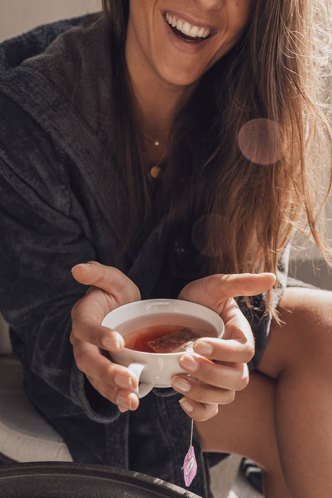 Bilder aus der Sportalm Frau im Bademantel hält eine Tasse Tee und lächelt
