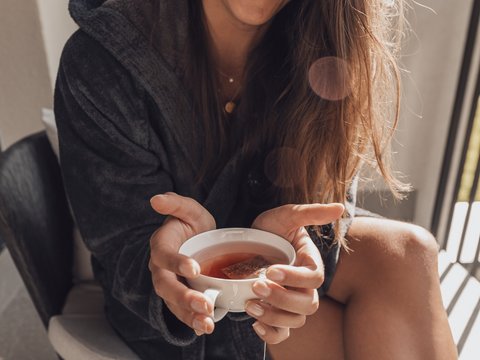 Bilder aus der Sportalm Frau im Bademantel hält eine Tasse Tee und lächelt