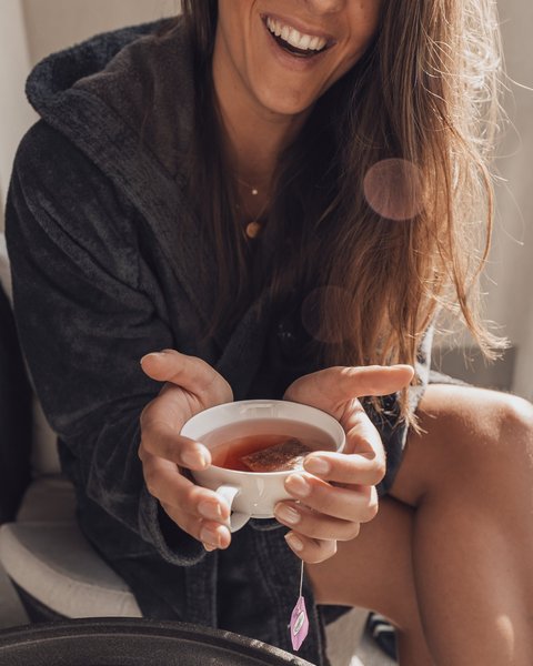 Bilder aus der Sportalm Frau im Bademantel hält eine Tasse Tee und lächelt