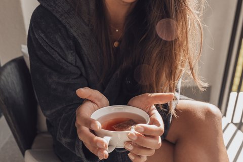 Bilder aus der Sportalm Frau im Bademantel hält eine Tasse Tee und lächelt