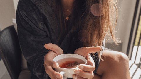 Bilder aus der Sportalm Frau im Bademantel hält eine Tasse Tee und lächelt
