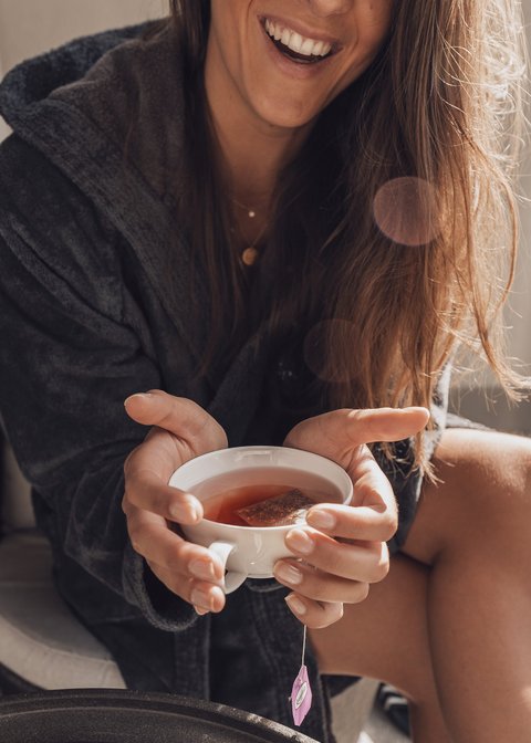 Bilder aus der Sportalm Frau im Bademantel hält eine Tasse Tee und lächelt