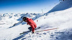 Hiking hotel in Pitztal: nature adventurers, ahoy! Skier in red jacket skiing on snowy sunny mountain slope