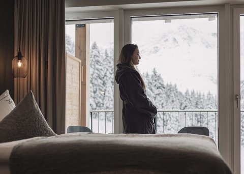 Pictures from Sportalm Woman in robe looking out hotel window at snowy mountain landscape