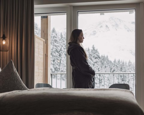 Bilder aus der Sportalm Frau im Bademantel blickt aus Hotelzimmer auf verschneite Berge