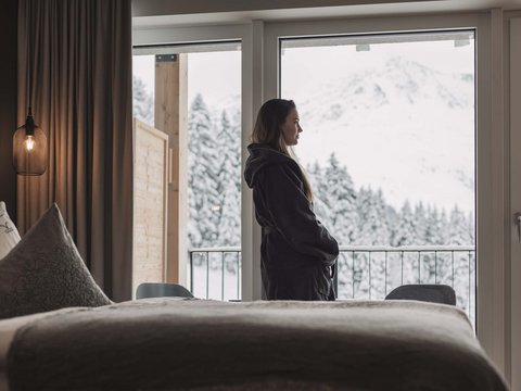 Pictures from Sportalm Woman in robe looking out hotel window at snowy mountain landscape
